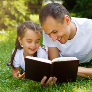father and daughter on grass reading a Bible